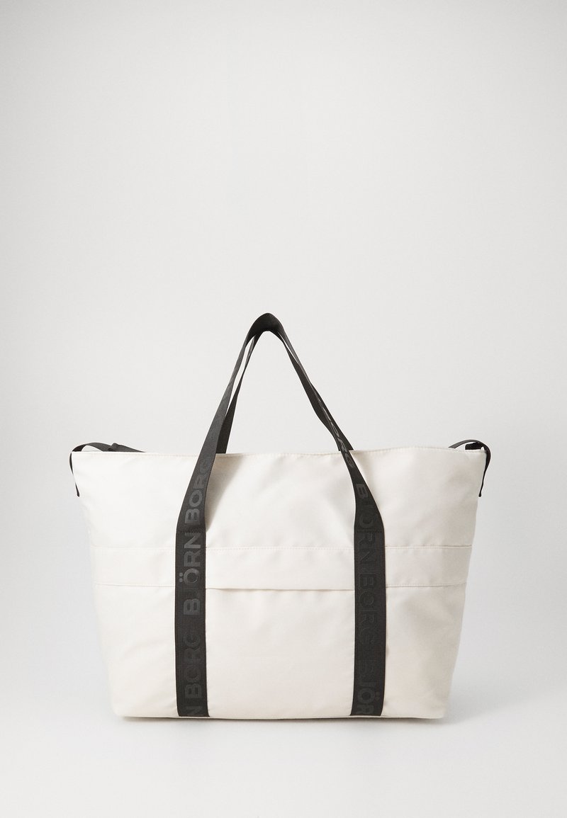 Bolsa de tela blanca con un diseño estructurado, asas negras en contraste con texto en relieve, y un bolsillo exterior plano.