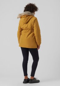 Yellow padded jacket with fur-trimmed hood, elastic waist, and kangaroo pockets. Paired with black leggings and black platform shoes.