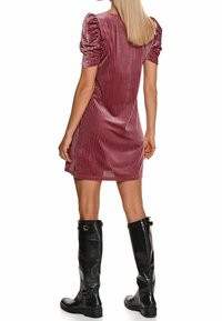 Kurzes pinkfarbenes Samtkleid mit vertikalen Streifen, gepufften Ärmeln und geradem Schnitt, kombiniert mit knielangen schwarzen Lederstiefeln.