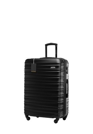 Valise rigide noire avec texture à rainures horizontales, poignée télescopique et quatre roues. Comprend une étiquette de prix attachée.