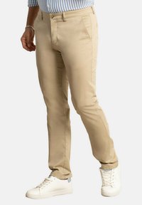 Pantalones de algodón beige con pierna recta, que cuentan con bolsillos frontales, cremallera y cierre de botón, combinados con zapatillas blancas.