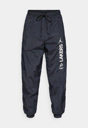 Jogging léger bleu marine, avec une ceinture élastique à cordon de serrage, des poches latérales et des logos imprimés blancs sur la jambe gauche.