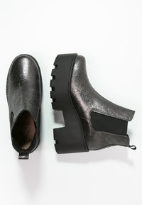 Botas de tobillo metálicas negras con un acabado texturizado, paneles laterales elásticos bajos y una suela de plataforma gruesa negra.