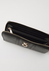 Black wallet with a textured finish, gold zipper, and a silver hardware accent. Interior compartments include card slots and a zip pocket.