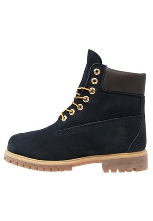Navy-Suede-Ankle-Boots mit einem braunen Lederkragen, goldenen Ösen und kontrastierenden gelben Schnürsenkeln auf einer robusten, beige Gummisohle.