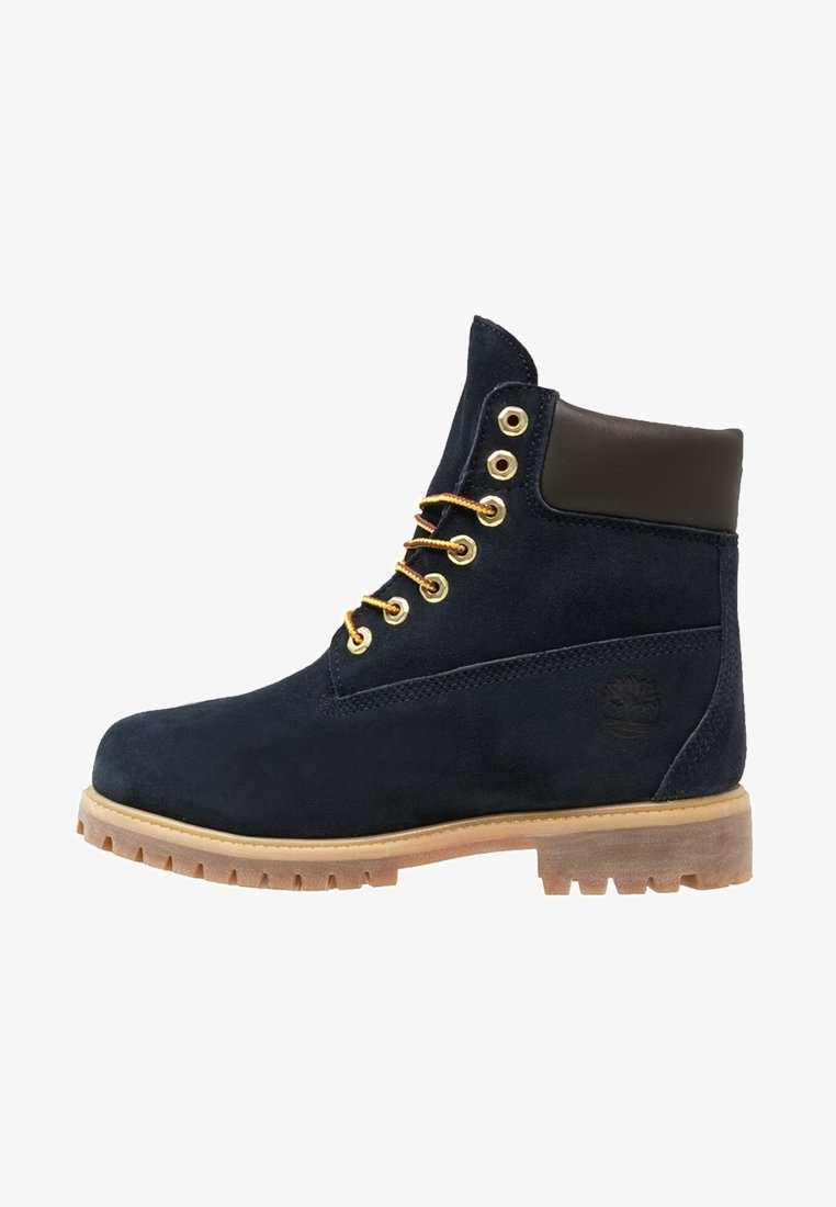 Navy suede ankle boots with a brown leather collar, gold eyelets, and contrasting yellow laces on a rugged tan rubber sole.