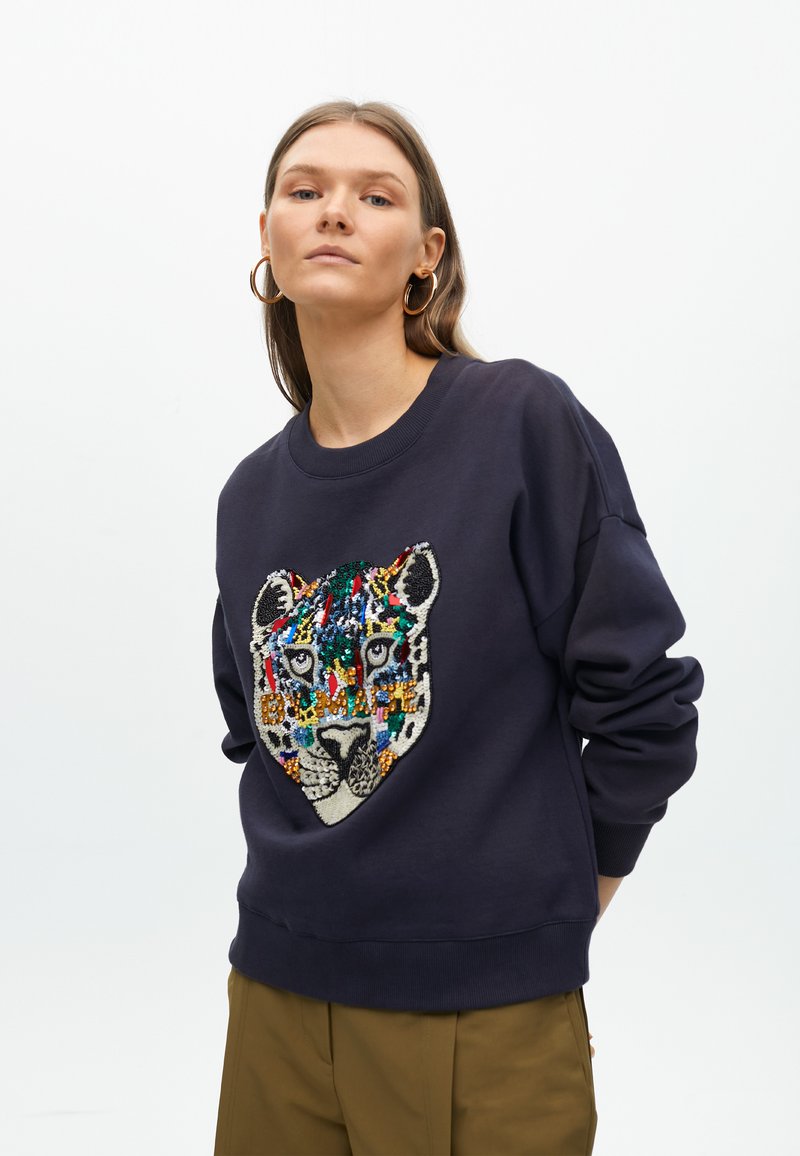Sudadera azul marino con un diseño de cara de leopardo colorido hecho de cuentas en la parte frontal. Presenta un cuello y puños acanalados, y un corte relajado.