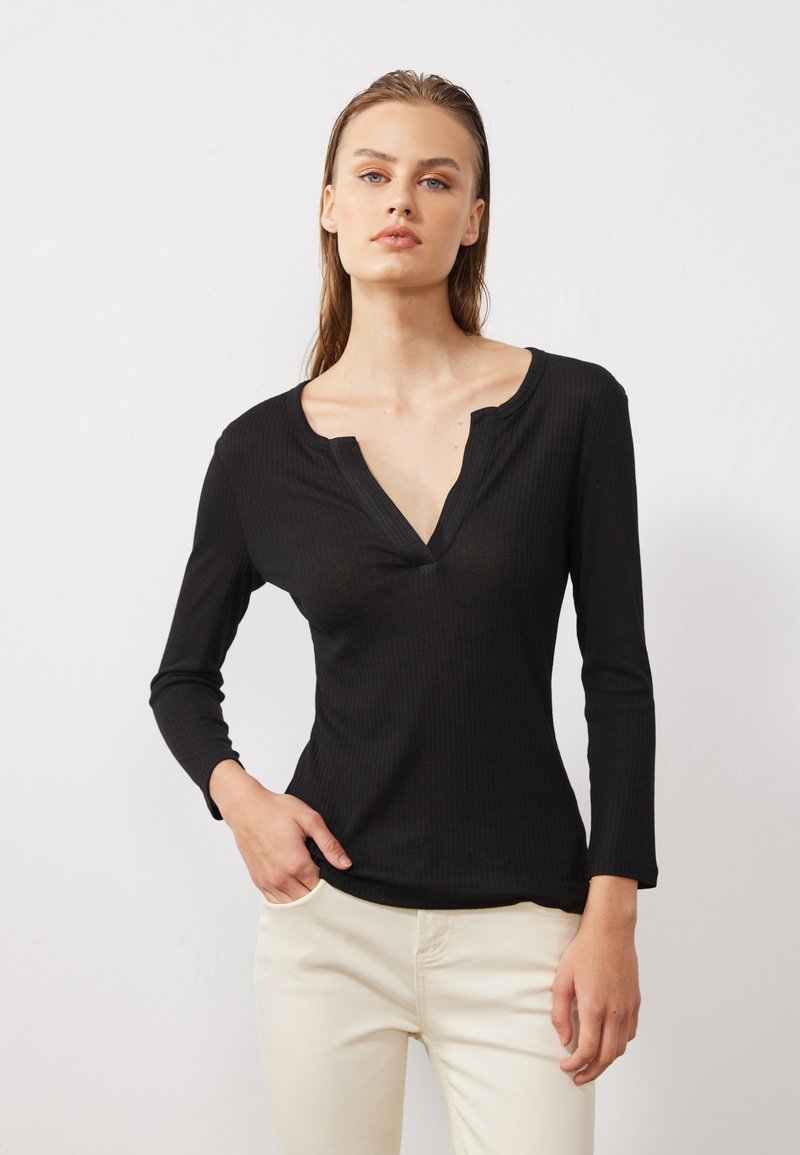 Haut noir à manches longues côtelé avec un décolleté en V. Il présente un design ajusté et une texture douce. Associé à un pantalon de couleur crème.