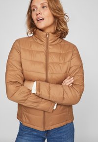 Pruun puffjakker kõrge kraega ja lukuga. Omab horisontaalseid tikandeid ja valgeid ribakrae.