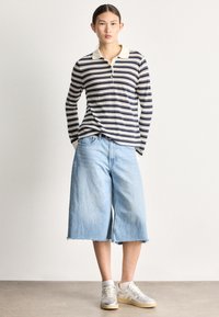 Tricou polo cu mânecă lungă cu dungi în nuanțe navy și crem, combinat cu pantaloni scurți largi din denim albastru deschis cu tivuri destrămate și adidași neutri.