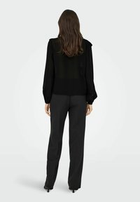 Sort, gennemsigtig bluse med lange ærmer, en struktureret mønster og en løs silhuet. Kombineret med sorte, skræddersyede bukser, hvilket skaber et monokromt look.