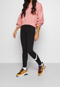Rosa oversized sweatshirt med puffärmar, åkt med svarta leggings som har en vit logotyp, och flerfärgade träningsskor med strukturerade sulor.