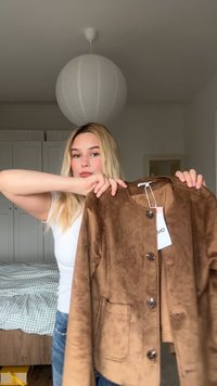 Brown faux suede jacket with round neckline, button closure, and side pockets, displayed by a person against a neutral background.