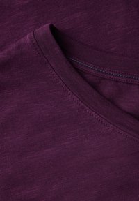 Tričko s výstřihem do V v bohaté fialové barvě, s texturovanou tkaninou a kontrastním švem kolem výstřihu. Měkký, lehký materiál.