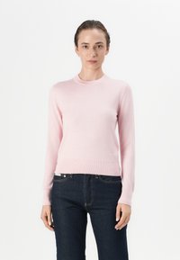Pullover rosa chiaro realizzato in un tessuto morbido, con scollo rotondo, maniche lunghe e orlo a costine, abbinato a jeans scuri.