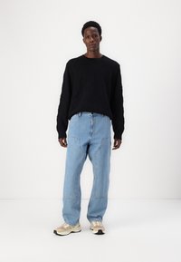 Sort strikket sweater med diamantmønster, parret med lysblå løse jeans med patchworkdetaljer og beige sneakers.