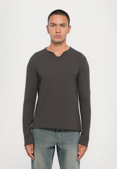 Chemise à manches longues gris foncé avec un col henley, patte de boutonnage à trois boutons et coupe ajustée. Texture douce, associée à un jean bleu clair.