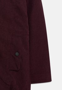 Wrzosowa kurtka z tkaniny o teksturowanym wykończeniu, z boczną kieszenią z czarnym guzikiem i starannie przeszytymi szwami.