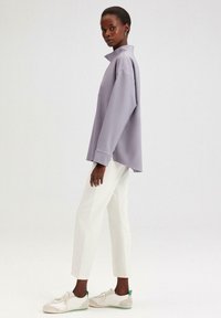 Levendula színű oversized pulóver magas gallérral, fehér, slim-fit nadrággal és zöld kiegészítőkkel rendelkező világos sportcipőkkel párosítva. Sima szövet textura.