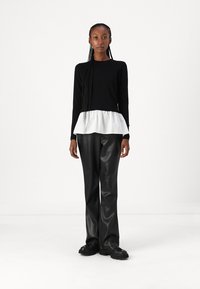 Top lungo nero a maniche lunghe con orlo peplum bianco, abbinato a pantaloni in pelle sintetica nera e scarpe chunky nere. Tessuto dalla consistenza liscia.