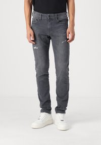 Pantalones vaqueros gris de corte ajustado, con detalles desgastados y un diseño clásico de cinco bolsillos. Combinados con zapatillas deportivas blancas.