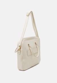 Beige læder håndtaske med guldbeslag, dobbelte håndtag og en aftagelig skulderrem. Struktureret design med en flad, glat tekstur.