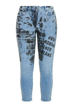 Jasnoniebieskie obcisłe dżinsy z czarnymi wzorami tie-dye i napisem "Busy making other plans" nadrukowanym na prawej udzie.