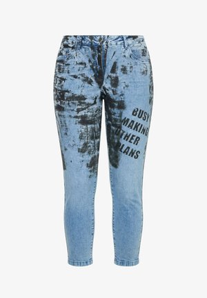 Hellblaue Skinny-Jeans mit schwarzen Tie-Dye-Mustern und dem Text „Busy making other plans“ auf dem rechten Oberschenkel gedruckt.