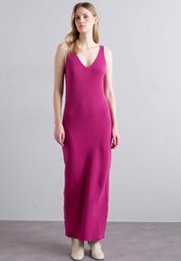 Robe longue ajustée de couleur magenta en tissu côtelé. Elle présente un décolleté en V profond et de larges bretelles. Texture lisse, longueur jusqu'aux chevilles.