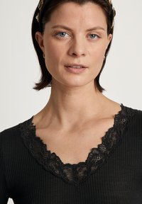 Top nero a coste con scollatura in pizzo ondulato. Il tessuto è morbido, con una vestibilità slim e una sottile texture.