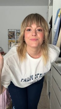 Hvid oversized t-shirt med "PALM SPRINGS" trykt i marineblå. Mørk marineblå bukser. Håret er bølget med bløde striber. Tilbehør inkluderer øreringe.