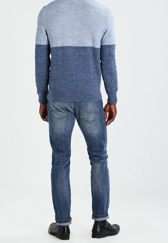 Blue knit sweater with textured design, graduated shades from light to dark, paired with light blue jeans and black shoes.