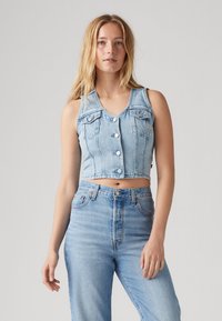 Světle modrá džínová zkrácená vesta s výstřihem do V, bez rukávů, předním zapínáním na knoflíky a dvěma náprsními kapsami. Plochý přední díl, pohodlný střih.