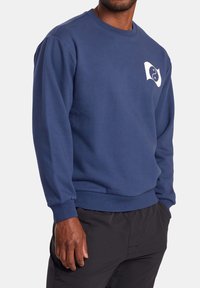 Sweat-shirt bleu marine en tissu doux, avec col rond, poignets côtelés et un logo blanc imprimé sur la poitrine.