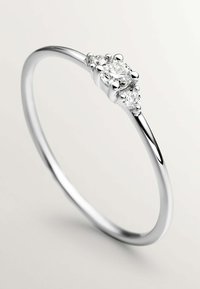 Anillo de plata con un diamante redondo central, flanqueado por dos diamantes más pequeños, con una banda lisa y un acabado pulido.