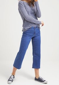 Navy- und weiß gestreiftes Langarmoberteil mit lockerer Passform, kombiniert mit verkürzten blauen Jeans und schwarzen Segeltuchschuhen. Schlichte Gestaltung.