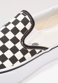 Cipele na vezivanje od platna s crno-bijelim kariranim uzorkom, crnim akcentima, bijelim gumenim đonom i Vans logom sa strane.