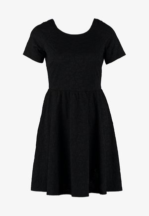 Czarna sukienka z krótkim rękawem, dopasowana w talii z rozkloszowanym dołem. Materiał wydaje się mieć fakturę. Dobranie czarne rajstopy i płaskie buty.