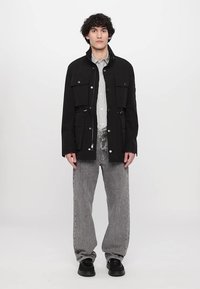 Zwarte fieldjack met meerdere zakken, drukknoopsluitingen en verstelbare trekkoorden. Draag het over een gestreept shirt en combineer het met grijze jeans.