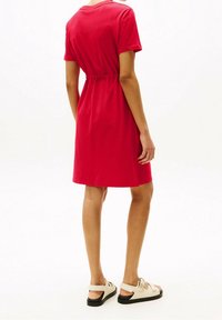 Vestido de camiseta de algodón rojo con un corte relajado, cintura elástica y mangas cortas. Combinado con sandalias ligeras con suela negra.