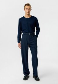 Marineblauwe overhemd met lange mouwen, gecombineerd met marineblauwe pantalon, met een riem en een recht model. Afgemaakt met zwarte schoenen.