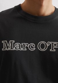 Zwart katoenen t-shirt met een opvallende zilveren patroon "Marc O'P" grafiek op de voorkant, met een klassieke ronde hals en korte mouwen.