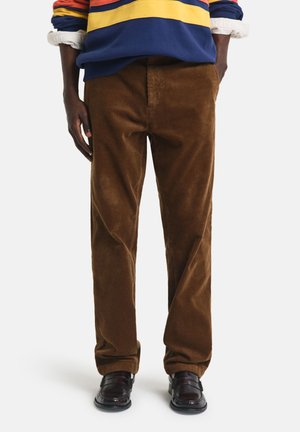 Brown corduroy pants with wide legs, featuring vertical ribbed texture. Paired with a colorful striped sweatshirt and black shoes.