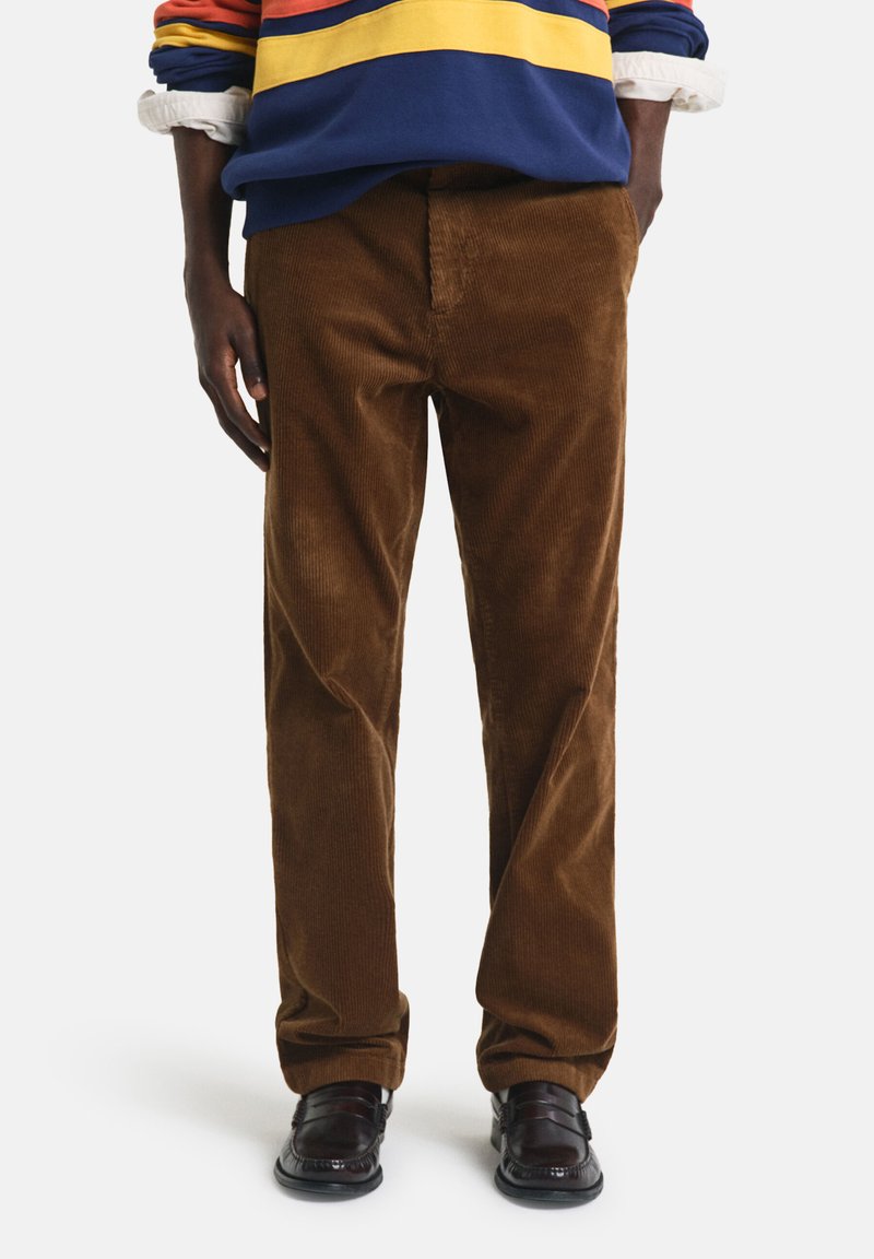 Brown corduroy pants with wide legs, featuring vertical ribbed texture. Paired with a colorful striped sweatshirt and black shoes.