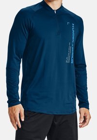 Navy long-sleeve athletic shirt with a quarter-zip, lightweight fabric, and side panel detailing. Features white Under Armour text on the front.