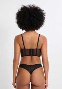 Schwarzes Dessous-Set mit einem transparenten Mesh-BH mit verstellbaren Trägern und Hakenverschluss, kombiniert mit passenden transparenten Mesh-Slips.