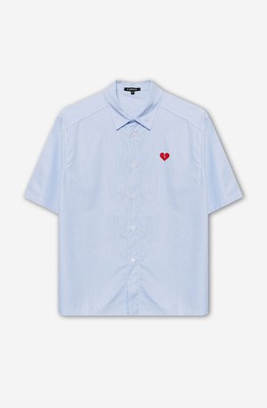 Camisa de botão de mangas curtas em tecido riscado azul claro, apresentando um patch de coração vermelho no lado esquerdo do peito. Gola clássica e um corte descontraído.