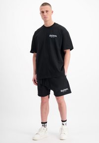 Zwarte T-shirt met korte mouwen en bijpassende shorts, beide gemaakt van zachte stof, met een wit tekstlogo. Sneakers hebben een chunky ontwerp.