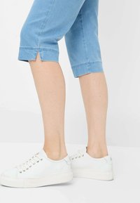 Pantaloni in denim azzurro chiaro, a vita alta e cropped, con una leggera apertura all'orlo, abbinati a sneakers bianche con lacci e suola spessa bianca.