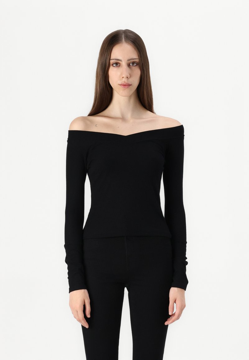 Svart off-shoulder topp med lange ermer, tettsittende design og subtil v-hals. Laget av myk, elastisk stoff. Kombinert med svarte bukser.